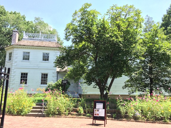 Side view of the mansion. A garden surrounds steps leading up to a side entrance of the two story structure. The exterior is painted white.